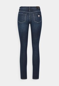 Tummansiniset skinny-farkut, jotka on valmistettu denimestä, ja joissa on sileä pinta, takataskut sekä pieni kolmion muotoinen logo vyötärön lähellä.