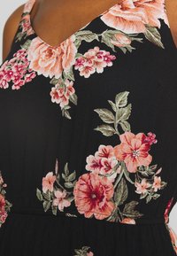 Robe en tissu noir avec décolleté en V, ornée de grandes broderies florales roses et rouges ainsi que de feuilles vertes. Texture douce, design ajusté.