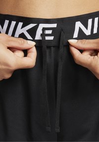 Svarta sportshorts med en vit Nike-logotyp på midjebandet. Har dragsnören för justerbarhet. Texturerat tyg med en slät yta.