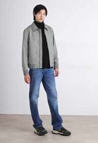 Grå og grønn stripet lett jakke over en svart polo, kombinert med blå jeans og svarte camo-sneakers. Enkelt design, casual passform.