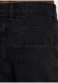 Jeans in denim nero che mostrano un primo piano della vita e della tasca posteriore. Le caratteristiche includono una texture resistente e cuciture pulite.