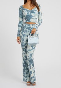 Dvoudílný outfit obsahující dlouhý rukáv crop top a rozšířené kalhoty s modrým květinovým potiskem na světlém pozadí. Doplňený světle modrou kabelkou.