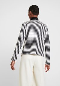 Maglione a righe nero e bianco, con scollo rotondo e maniche lunghe, caratterizzato da un design a maglia testurizzata e una vestibilità leggermente corta.