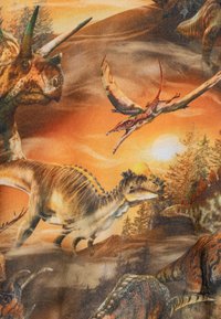 Diversi dinosauri colorati, tra cui un pterosauro volante, un triceratopo e uno stegosauro, si stagliano su uno sfondo di un infuocato tramonto arancione e un paesaggio boschivo.