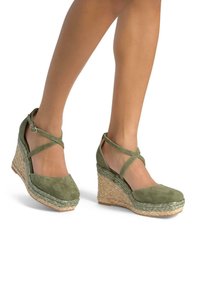 Sandali con zeppa in suede verde con fasce incrociate, dotati di una piattaforma in juta intrecciata. L'altezza del tacco è moderata e la suola è testurizzata.