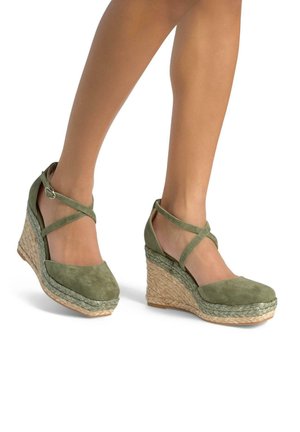 Sandali con zeppa in suede verde con fasce incrociate, dotati di una piattaforma in juta intrecciata. L'altezza del tacco è moderata e la suola è testurizzata.