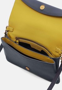 Lederhandtasche mit einem senfgelben Klappen und einem marineblauen Korpus. Verfügt über einen Magnetverschluss, eine innere Reißverschlusstasche und einen verstellbaren Riemen.