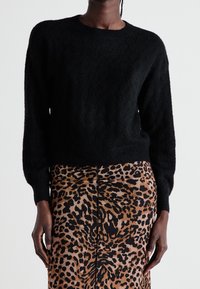 Svart texturerad tröja med rund hals och långa ärmar, i kombination med en brun leopardmönstrad kjol med en central söm och slät finish.