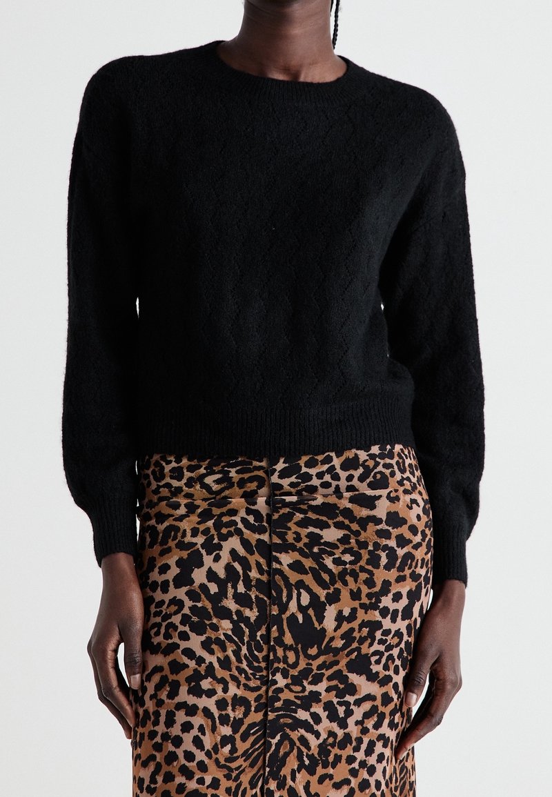Svart texturerad tröja med rund hals och långa ärmar, i kombination med en brun leopardmönstrad kjol med en central söm och slät finish.