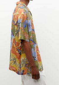Chemise à manches courtes avec col, aux couleurs vives—orange, vert, bleu—avec des motifs floraux tropicaux. Fabriquée en tissu léger, coupe décontractée.