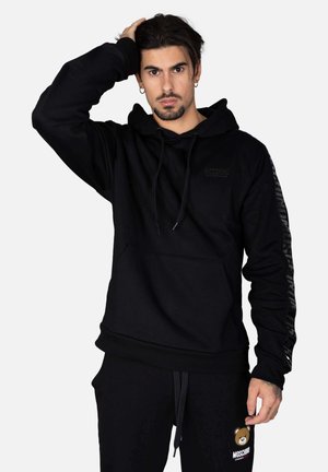 Felpa nera con cappuccio e cordini, tasca a marsupio e logo. Strisce nere texturizzate sulle maniche. Tessuto morbido con una vestibilità rilassata.