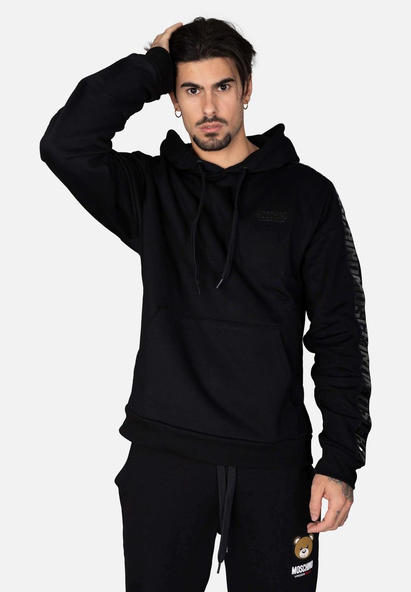 Felpa nera con cappuccio e cordini, tasca a marsupio e logo. Strisce nere texturizzate sulle maniche. Tessuto morbido con una vestibilità rilassata.