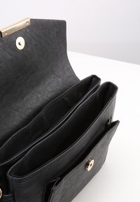 Pochette in pelle nera aperta che mostra tre scomparti principali e chiusure a scatto magnetico, posata su una superficie bianca.