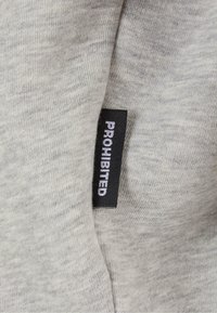 Tela gris con una textura suave. Se ha cosido una etiqueta negra que dice "PROHIBIDO" en la tela. Enfoque en el diseño de punto sin costuras.