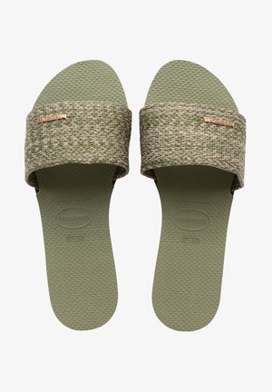 Zielone sandały na płaskiej podeszwie z teksturą, z plecionym paskiem z różowymi akcentami i logo w kolorze różowego złota. Elastyczna gumowa podeszwa z rowkowanym wzorem dla lepszej przyczepności.
