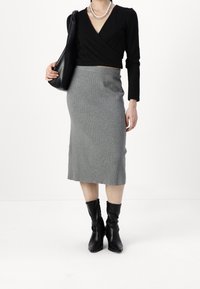 Svart omlott-topp med lång ärm, grå ribbad pennkjol, svarta läderstövlar till mitten av vaden och en svart väska. Texturerat tyg med figurnära silhuett.