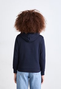 Hanorac cu glugă de culoare albastru marin, fabricat dintr-un material moale, cu manșete și tiv cu nervuri, având un design simplu, văzut din spate.