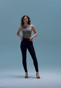 Pilkas be rankovių bodis su lygiu paviršiumi, derinamas su juodais aukšto liemens džinsais ir juodomis aukštakulnėmis basutėmis. Vienodas mėlynas fonas.