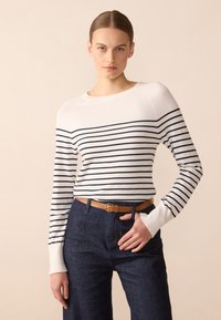 Pull en tricot rayé blanc et marine, avec un col rond et des manches longues. Assorti à un jean skinny en denim foncé taille haute et une ceinture marron.