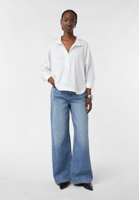 White, long-sleeve collared shirt with a relaxed fit, paired with blue wide-leg denim jeans. Smooth texture, minimal detailing. Black shoes.