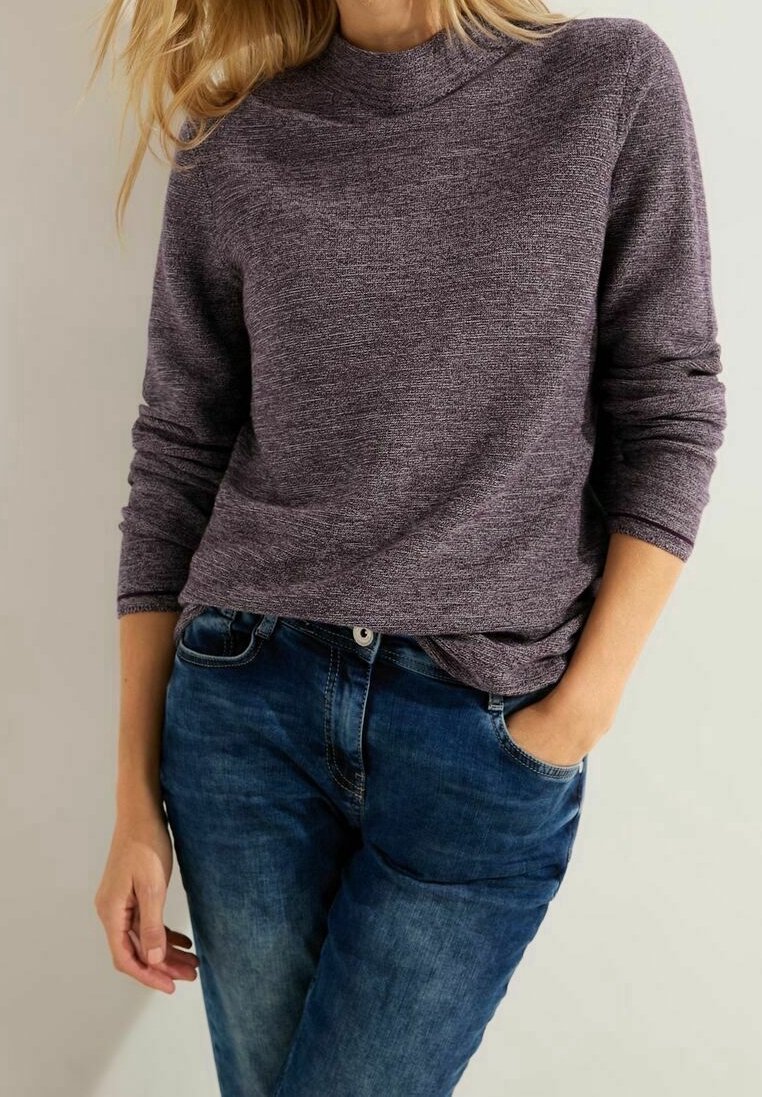 Lila strukturierte Langarmbluse mit hochgeschlossenem Kragen, kombiniert mit blauen Jeans. Die Bluse hat einen lässigen Schnitt und subtile Farbvariationen.