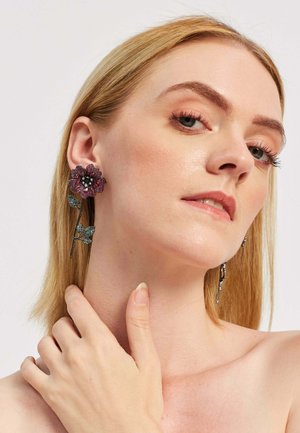 Earrings featuring a large, purple flower with crystal accents, complemented by green leaf details on a dark metal stem.