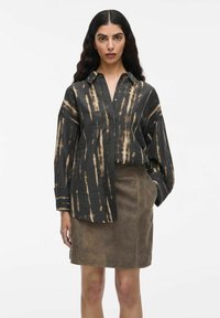 Schwarzes Hemd mit hellbraunen Batikstreifen, mit Kragen und lockerer Passform. Kombiniert mit einem engen Rock aus braunem Wildleder, der Textur und Design hervorhebt.
