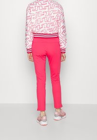 Růžové upnuté kalhoty, hladká látka, minimální pružnost. V kombinaci s vzorovanou bílou bundou s červenými designovými liniemi a žebrovanými manžetami.