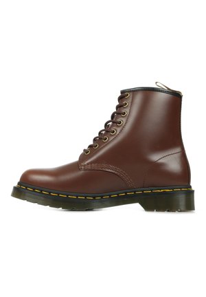 Bottine en cuir marron avec un bout rond, présentant des accents noirs, des œillets dorés et un détail de couture jaune le long de la semelle.