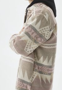 Giacca decorata con design geometrici in toni di rosa tenue, beige e grigio. Realizzata in tessuto testurizzato con una vestibilità comoda.