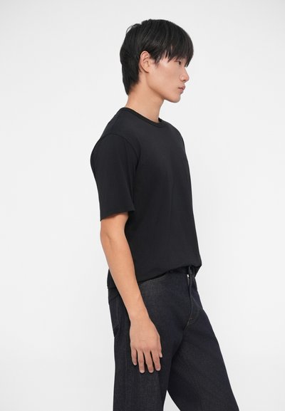 Camiseta de algodón negra con mangas cortas, escote redondo y un ajuste relajado, combinada con jeans de denim oscuro. Diseño sencillo, sin patrones visibles.