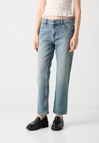 Jasnoniebieskie dżinsy o prostym kroju z wyblakłym wykończeniem, pięć kieszeni, z metalowym zapięciem, w połączeniu z czarnymi, platformowymi mokasynami.