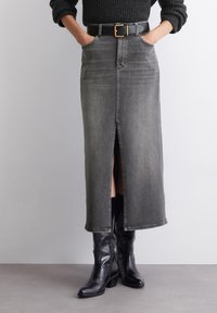 Gray denim midi skirt with a front slit, five pockets, and belt loops. Styled with a black belt and knee-high black boots.