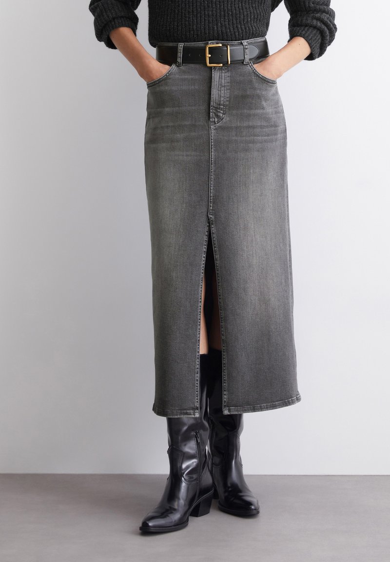 Gray denim midi skirt with a front slit, five pockets, and belt loops. Styled with a black belt and knee-high black boots.