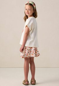T-shirt blanc à manches courtes avec un graphique de cerises, associé à une jupe évasée ornée d'un imprimé de cerises colorées et à des sandales marron.