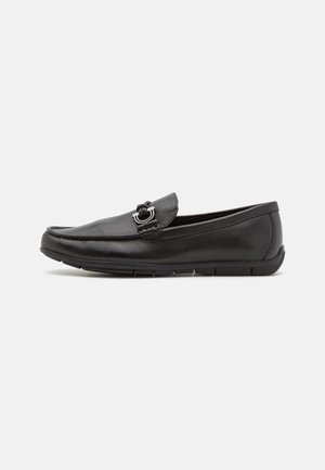 Mocassin en cuir noir avec détail mors argenté et semelle en caoutchouc basse, vu de côté sur fond blanc.