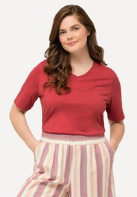 Červené tričko s krátkým rukávem a výstřihem do V vyrobené z měkké látky, spárované se světle růžovými a krémovými pruhovanými kalhotami s elastickým pasem.