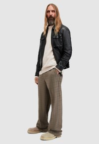 Schwarze Lederjacke, beiger Strickpullover, karierte braune Hose und hellfarbene Clogs. Insgesamt eine entspannte Passform und mehrlagiger Look.