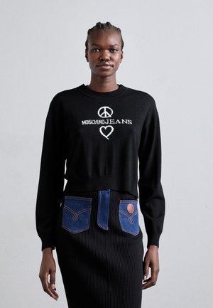 Un pull en tricot noir avec le logo "MOSCHINOJEANS" et un symbole de paix, associé à une jupe noire côtelée avec des poches en denim bleu.