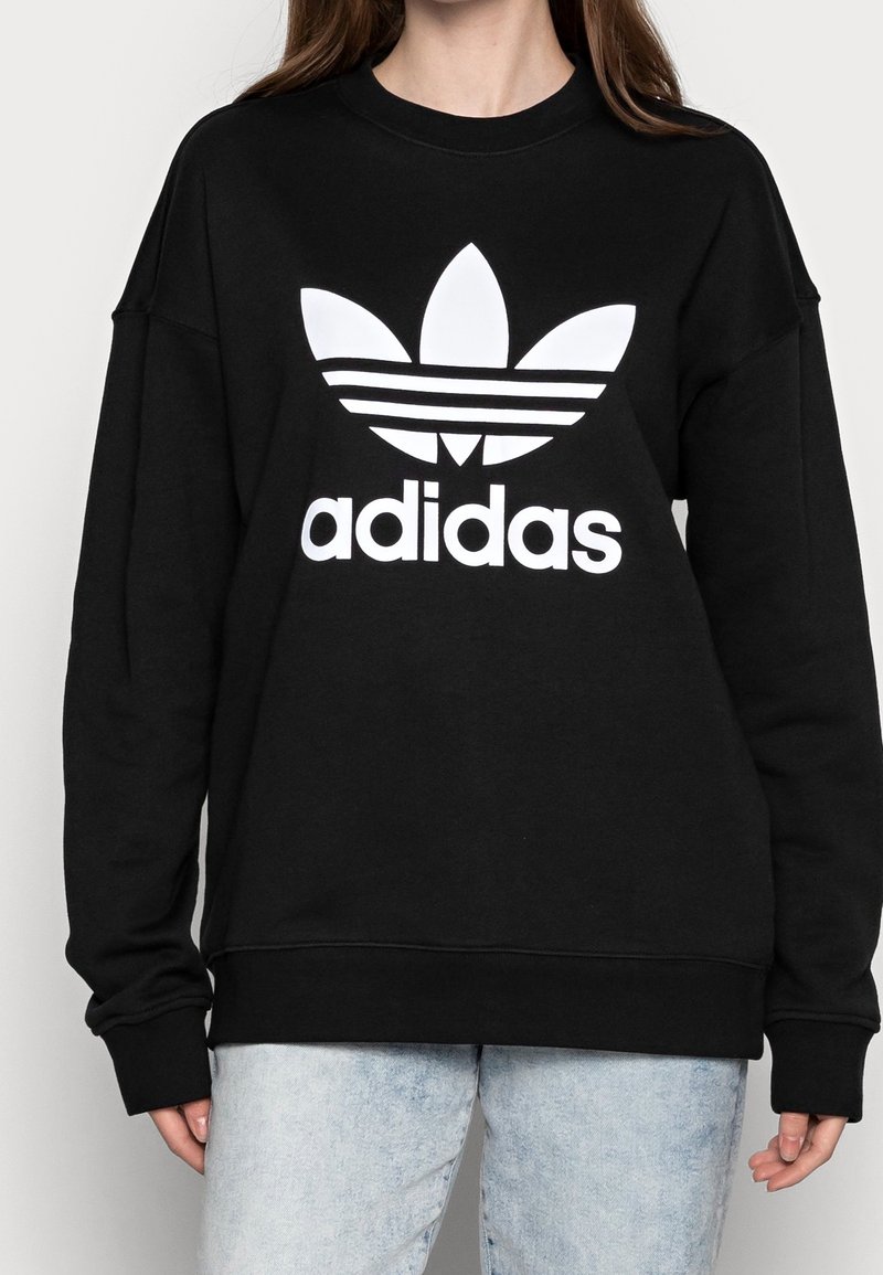 Sudadera negra de algodón, que presenta un gran logo blanco de Adidas con el diseño de trébol y tres franjas horizontales.