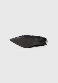 Sort ruskinds sko med spids tå og et elegant design, der har en buet silhuet og en blank sort hæl. Sålen er struktureret.