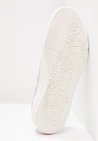 Sneaker con suola in gomma bianca testurizzata caratterizzata da un logo pronunciato, accenti grigio chiaro e un motivo di battistrada intricata.