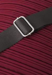 Tissu plissé bourgogne avec une large ceinture noire dotée d'une boucle rectangulaire en argent mise en avant au centre.