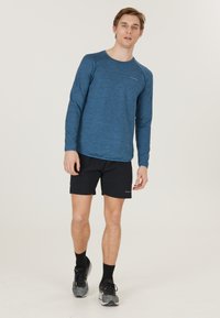 Langærmet blå meleret træningsshirt med rund halsudskæring, sorte shorts og grå løbesko. Glat stof med en struktureret overflade.