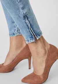 Světlé modré džíny s zipy na kotnících, kombinované s béžovými lodičkami na vysokém podpatku v jemné textuře.