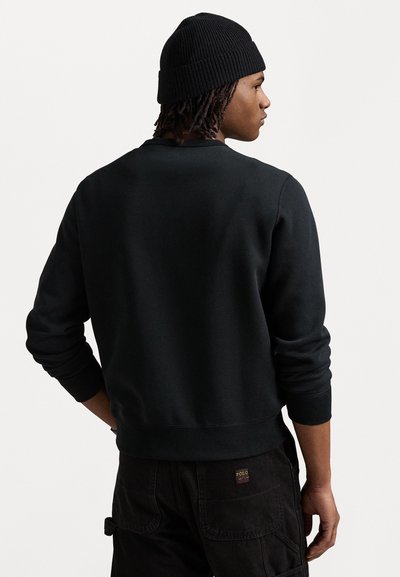 Sort sweatshirt med ribbede manchetter og bund, lavet af blødt materiale. Bæres med en sort ribbet beanie, der viser en afslappet pasform bagfra.