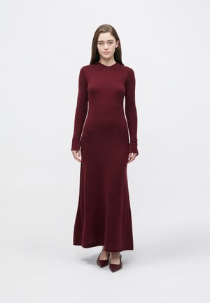 Burgundské pletené šaty s dlouhými rukávy, přiléhavým živůtkem a rozšířeným lemem. Hladká textura a kulatý výstřih. Nosit s ladícími lodičkami s špičatou špičkou.