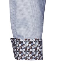 Hellblaues Hemd aus strukturiertem Stoff, mit einem floral bedruckten Manschette in Brauntönen, Blau und Weiß.