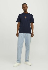 Mørkeblå bomulds t-shirt med et lille multicoloreret grafik på brystet. Sammen med lyseblå denimjeans og hvide sneakers.