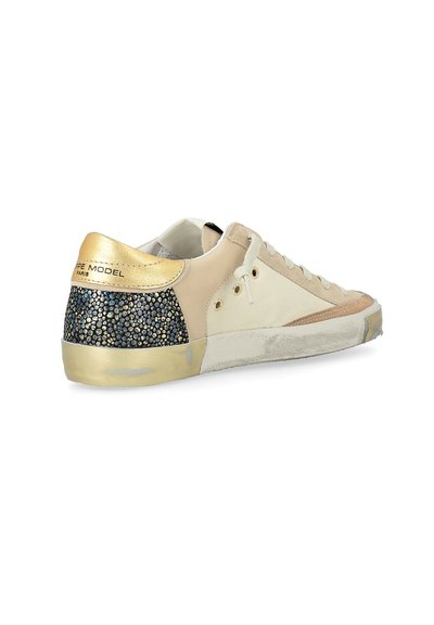 Baskets basses beiges avec talon métallique doré et patch noir à motifs, lacets blancs et semelle blanche légèrement usée.